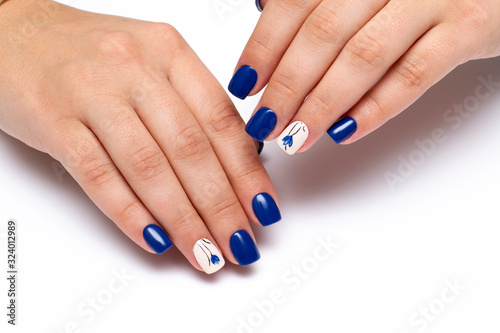Blue manicure with a beige ringless nail and painted flowers on short square nails. Gel coating of nails. Close-up.