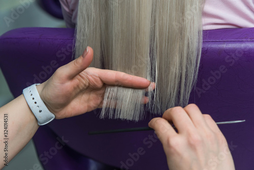 Young blondie in beauty salon. Professional hairdresser brushing straight client’s hair after hair care beauty procedures.