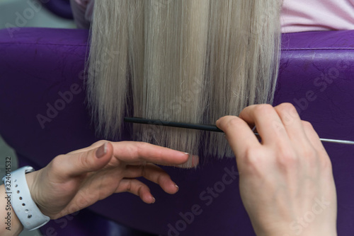 Young blondie in beauty salon. Professional hairdresser brushing straight client’s hair after hair care beauty procedures.