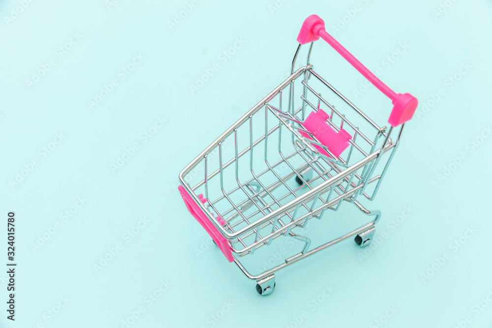 Small supermarket grocery push cart for shopping toy with wheels isolated on blue pastel colorful trendy background Copy space. Sale buy mall market shop consumer concept. Small supermarket grocery push cart for shopping toy with wheels isolated on blue pastel colorful trendy background Copy space. Sale buy mall market shop consumer concept.