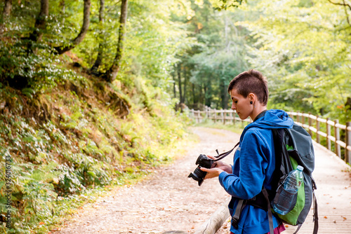 Serious youthful female hiker enjoying vacation and taking picture on professional camera while standing on wooden pathway in forest photo