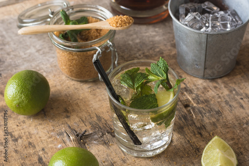 Overhead fresh limes and peppermint leaves placed on napkin and table near rum and brown sugar for mojito preparation