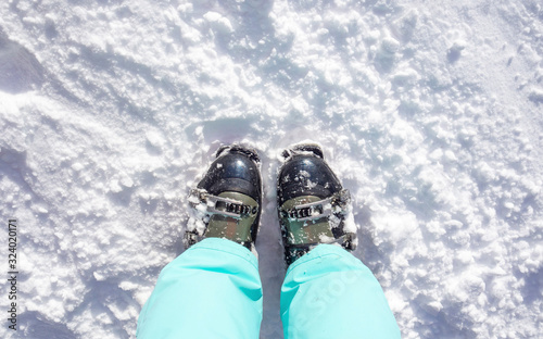 Feet in ski boots and in green pants. The concept of sport and relax. Copy space, snow background, top view