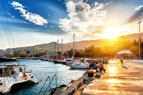 sea marina of resort city at sunset landmark with people walking along embankment against beautiful sky and setting sun background. Street wide view of yalta city in crimea. Town in mountains