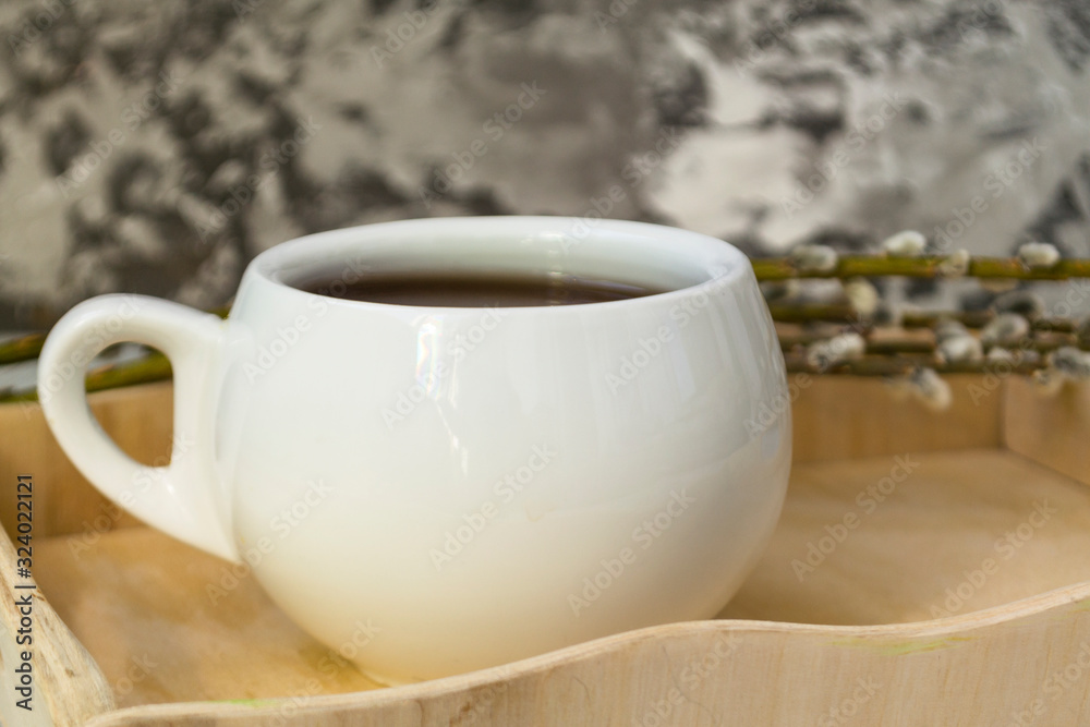 A willow twig with buds and a white cup of tea stands on a wooden tray. The concept of morning, breakfast A willow twig with buds and a white cup of tea stands on a wooden tray. The concept of morning, breakfast