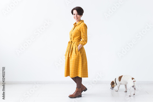 Cheerful young woman posing in a yellow dress with her beloved dog Jack Russell Terrier standing on a white background. The concept of casual wear.
