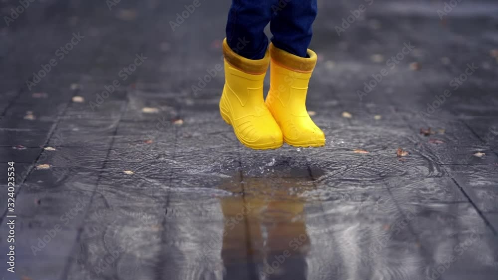 Happy child legs in yellow rubber boots dance and jump in small puddle