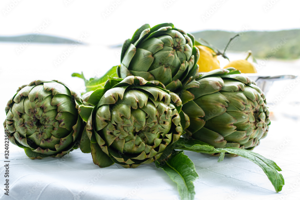 Obraz premium Cooking with fresh green artichokes heads, tasty vegetarian food, on open kitchen with sea view
