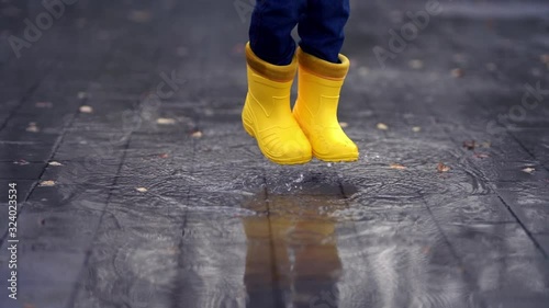 Happy child legs in yellow rubber boots dance and jump in small puddle