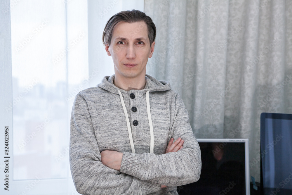 Fototapeta premium Portrait of handsome man dressed hoody, standing inside room with folded arms