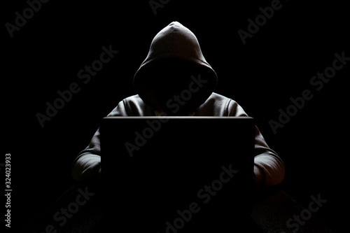 cybercrimp with a hidden face in the dark in front of a laptop, network security