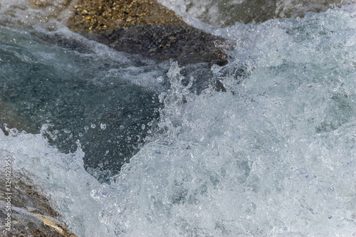 A close-up of a wave splashing over the mountain river cascade boulders: full frame stop motion shot © k.dei