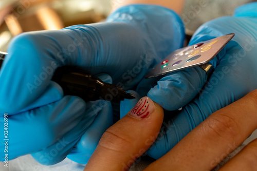 Close up of nail artist adding dots to design on short finger na photo