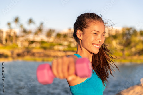 Fitness training Asian girl exercising arms workout with dumbbells doing lateral raises with free weights at outdoor beach summer park. Happy active healthy lifestyle.