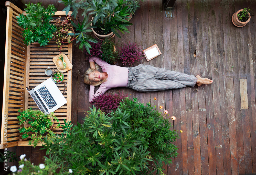 Top view of senior woman with laptop lying outdoors on terrace, resting. - obrazy, fototapety, plakaty 