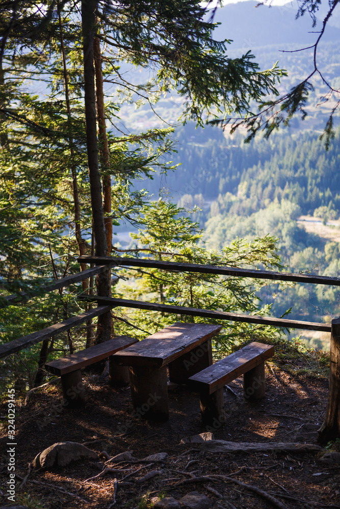 Observation deck on the eco-Hiking trail through the mountains of Bulgaria in the Rhodopes. Wooden benches and a table in the forest with a view of the panorama of the mountains Observation deck on the eco-Hiking trail through the mountains of Bulgaria in the Rhodopes. Wooden benches and a table in the forest with a view of the panorama of the mountains