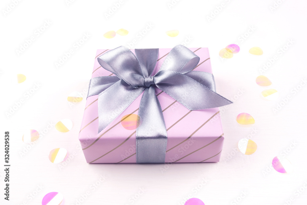One gift boxe with bow and confetti on a white background. Flat lay composition. Birthday, christmas, wedding or another holiday concept. One gift boxe with bow and confetti on a white background. Flat lay composition. Birthday, christmas, wedding or another holiday concept.