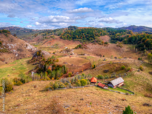 Village houses, autumn forest with colorful fall trees and and mountain green meadows. House, tree, hills.