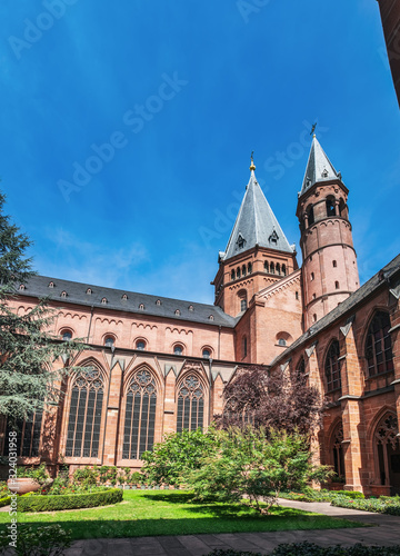 Mainz Cathedral with beautiful garden under blue cloudy sky, located in Old Town of Mainz, Germany. Red church bell towers.