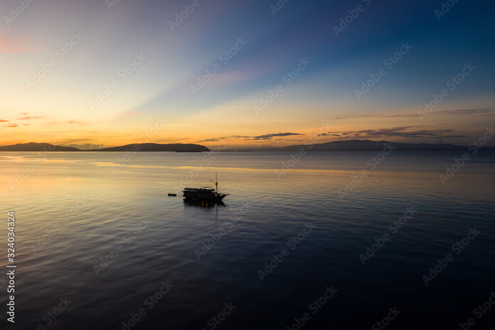 Sunrise silhouettes a diving live aboard ship in Raja Ampat, Indonesia. This region is thought to be the center of marine biodiversity and is a popular area for diving and snorkeling.