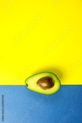 Green fresh avocado on isolated yellow and blue background. Vitamin, vegan food concept
