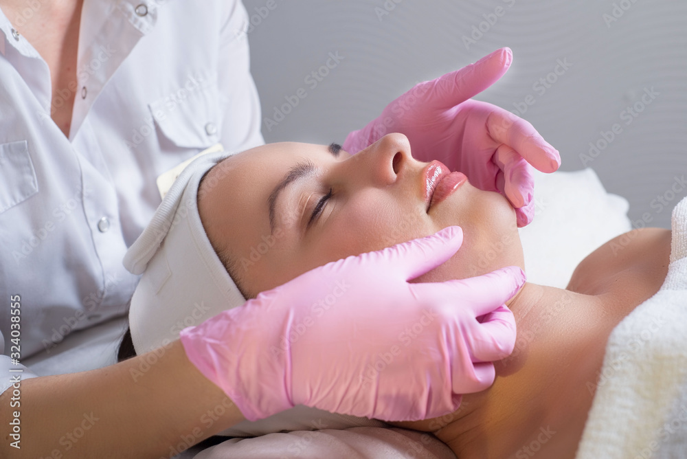 close-up, portrait of a young beautiful girl, with flawless skin, which the master masseur makes facial massage, in medical gloves. In a beauty salon close-up, portrait of a young beautiful girl, with flawless skin, which the master masseur makes facial massage, in medical gloves. In a beauty salon