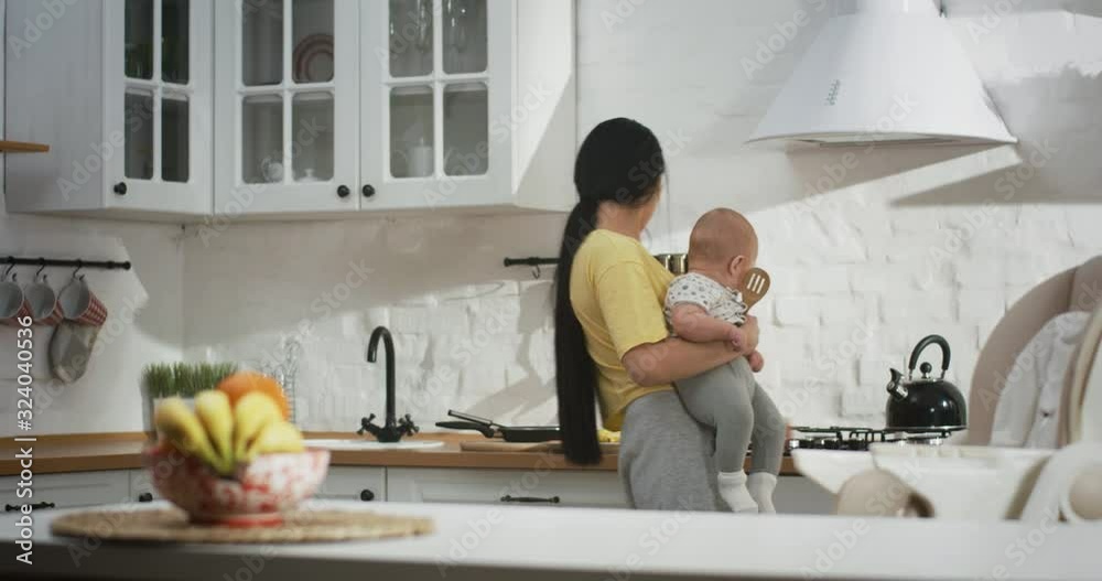 Young mother doing housework while holding baby Young mother doing housework while holding baby