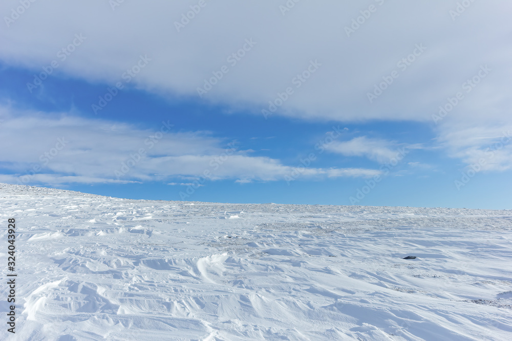 An scenic view of a moutain range in the winter with snowy slope under a majestic blue sky and some white clouds