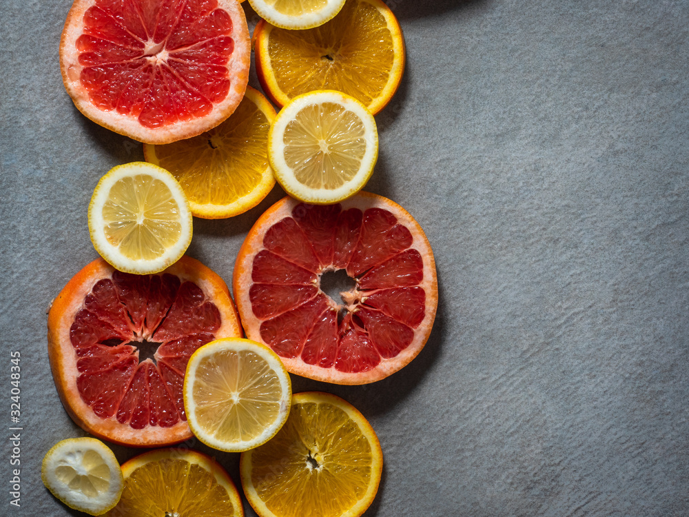Background of the round slices of the ripe various citrus with their peel closeup against grey background Background of the round slices of the ripe various citrus with their peel closeup against grey background