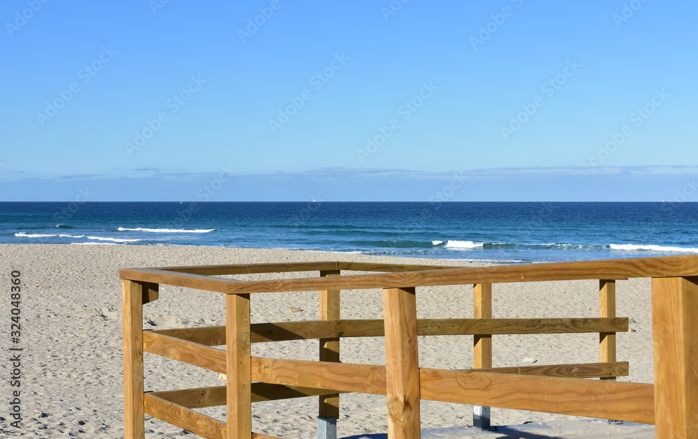 Summer landscape with beach and wooden handrail. Sea with waves and blue sky. Galicia, Spain. Summer landscape with beach and wooden handrail. Sea with waves and blue sky. Galicia, Spain.