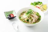 Vietnamese pho soup on white background. A classic authentic vietnamese food, this pho soup is served in a white bowl with chicken broth and lots of fresh garnishes such as cilantro and bean sprouts.