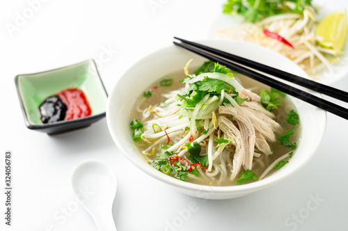 Vietnamese chicken pho noodle soup bowl. A classic authentic vietnamese food, this pho soup is served in a white bowl with chicken broth and lots of fresh garnishes such as cilantro and bean sprouts.
