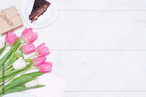 Bouquet of pink tulips, chocolate cake. pressent box on white wooden background. Copy space, close up. Mother's, women's day concept. Flat lay. photo