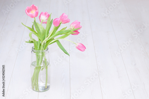 Pink tulips bouquet in glass vase on white wooden background. Copy space. Spring background  holiday  birthday concept.