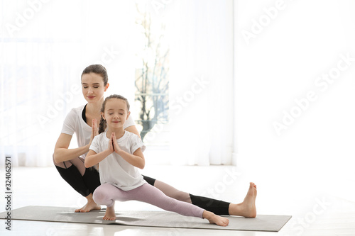 Young mother with little daughter practicing yoga at home