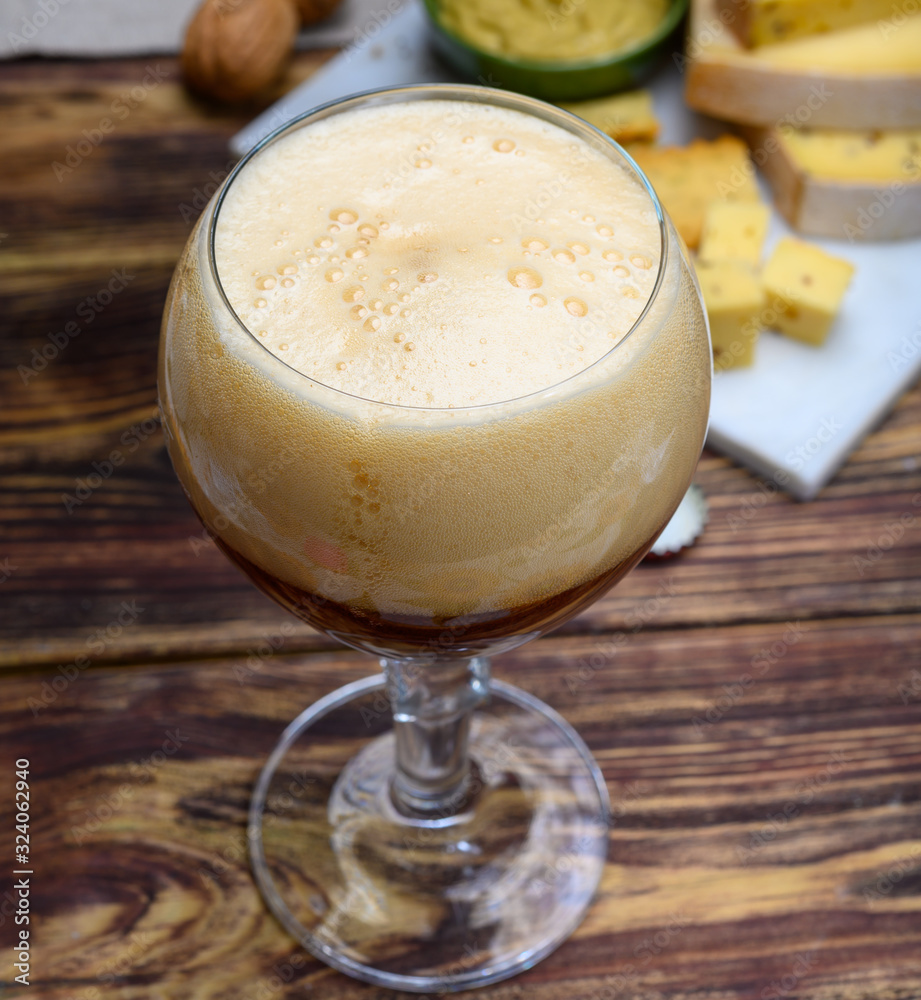 Glass of Belgian abbey brown beer and marble plate with cheeses made by monks from cow milk with fenugreek and mustard seeds Glass of Belgian abbey brown beer and marble plate with cheeses made by monks from cow milk with fenugreek and mustard seeds