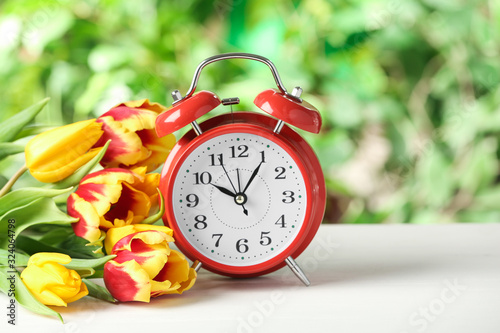Alarm clock and spring flowers on white wooden table. Time change concept