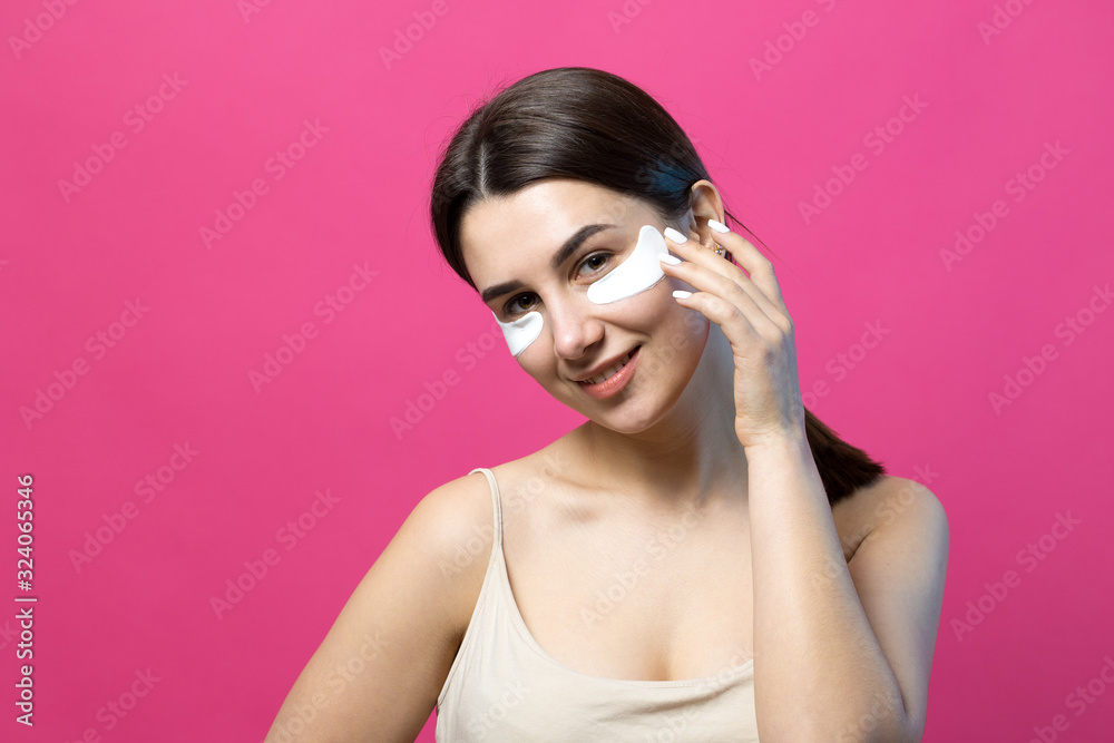 Close up portrait of pretty attractive girl with naked shoulders using patches under eyes. Standing over pink background. Close up portrait of pretty attractive girl with naked shoulders using patches under eyes. Standing over pink background.