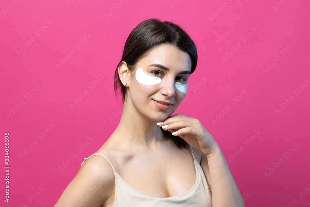 Close up portrait of pretty attractive girl with naked shoulders using patches under eyes. Standing over pink background. Close up portrait of pretty attractive girl with naked shoulders using patches under eyes. Standing over pink background.