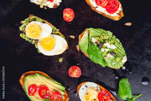 Sweet potato toasts with avocado, boiled eggs, tomatoes and sesame seeds on dark background. Healthy meal concept. Clean eating, Pescetarian food, top view