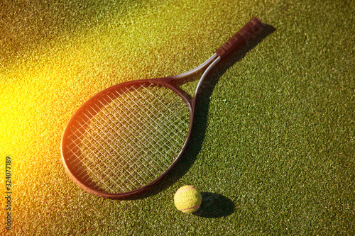 Tennis racket and yellow ball on the court with green grass and sunlight
