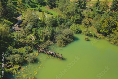 Принти на полотні Aerial photo of a beautiful green lake surrounded with trees, walking path and a small pier protruding into the lake on a sunny day