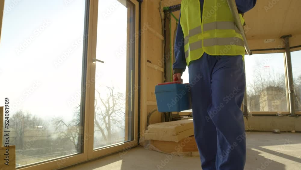 SLOW MOTION, CLOSE UP, LENS FLARE: Unrecognizable builder in blue coveralls leaves the beautiful wooden prefabricated house on a sunny evening. Contractor arrives to work in a cross-laminated house. SLOW MOTION, CLOSE UP, LENS FLARE: Unrecognizable builder in blue coveralls leaves the beautiful wooden prefabricated house on a sunny evening. Contractor arrives to work in a cross-laminated house.