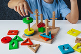 Child plays Montessori game. Kid collects wooden toy sorter. Multicolored geometric shapes, circle, square, triangle, rectangle.  Early childhood development