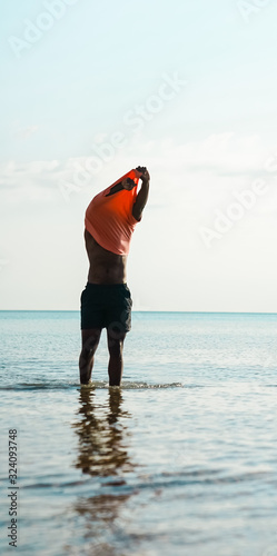 Male standing in lake wearing shorts taking off shirt