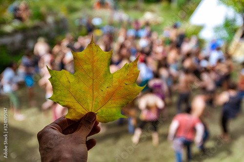 Closeup shot with shallow depth of field on a hand holding an autumnal leaf  against a blurry background of people doing guided yoga at earth festival
