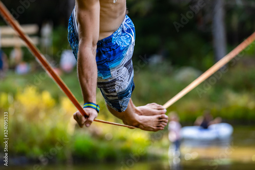 A close up and side view of a slim caucasian man practicing slacklining on a rope anchored over a pond. Risk, skill, muscle and strength concepts