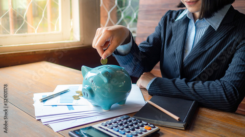 A business successful person is putting the coins in a blue piggy bank while working in the office. saving money is an investment for the future. Banking investment.