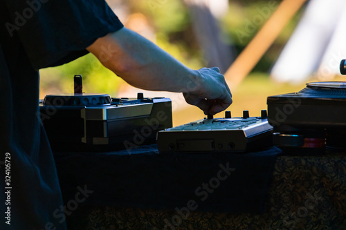A close up backlit selective focus shot on the hands of an EDM music performer using electronic CDJ decks. during a set at festival in nature