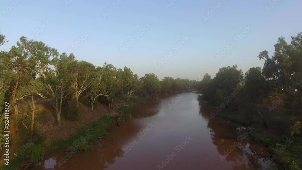 Drone flying above a riverbed and the trees lining it on either side and the beautiful clear blue sky Drone flying above a riverbed and the trees lining it on either side and the beautiful clear blue sky